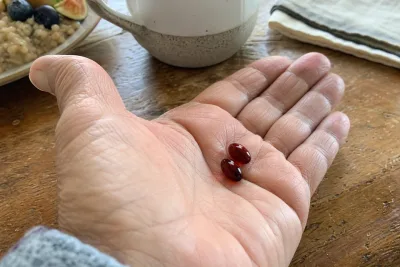 Two burgundy astaxanthin softgels in an older adult's hand at breakfast