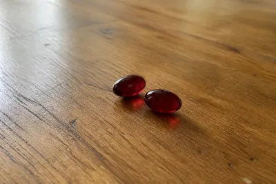 Two burgundy astaxanthin softgels resting on a wooden kitchen table