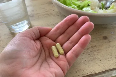 Two pale yellow citrus bergamot capsules in an older adult's hand at lunch